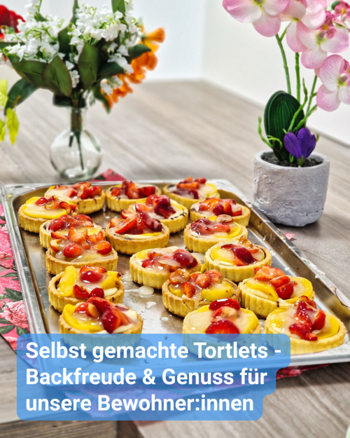 Ein Blech mit vielen kleinen, frisch belegten Obsttörtchen steht auf einem Tisch. Text: 'Selbst gemachte Tortlets - Backfreude & Genuss für unsere Bewohner:innen'.