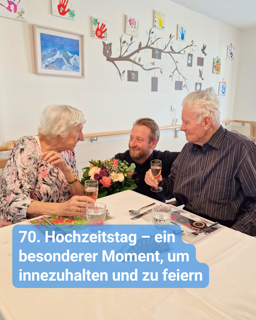 Ein älteres Ehepaar wird mit Blumen beglückwünscht. Sie stoßen gemeinsam mit einem Glas Sekt an. Bildbeschriftung: “70. Hochzeitstag – ein besonderer Moment, um innezuhalten und zu feiern“
